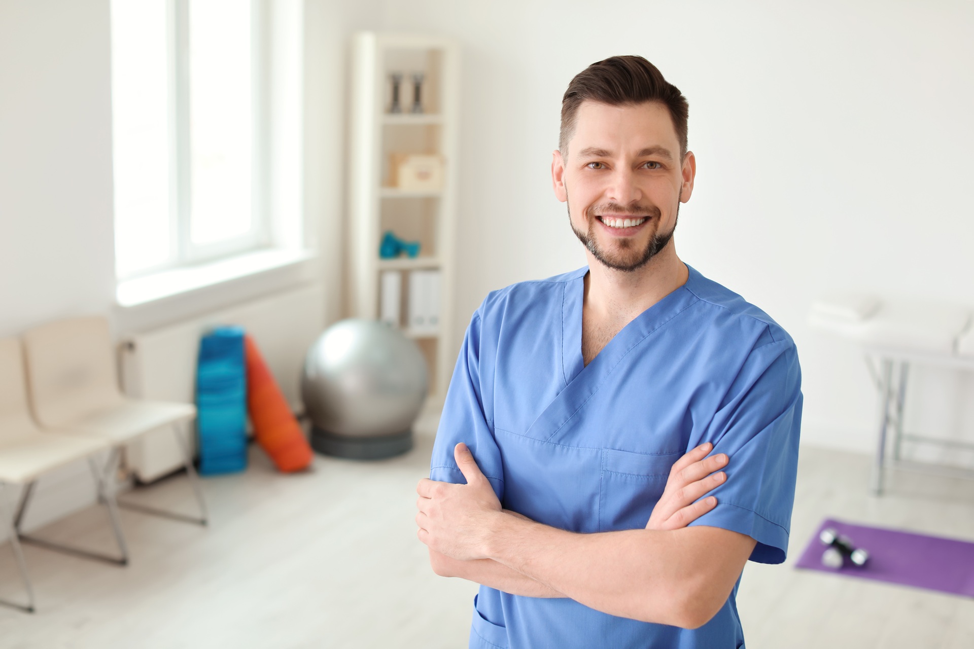 Physiotherapeut in Praxis mit verschränkten Armen | Therapieliege